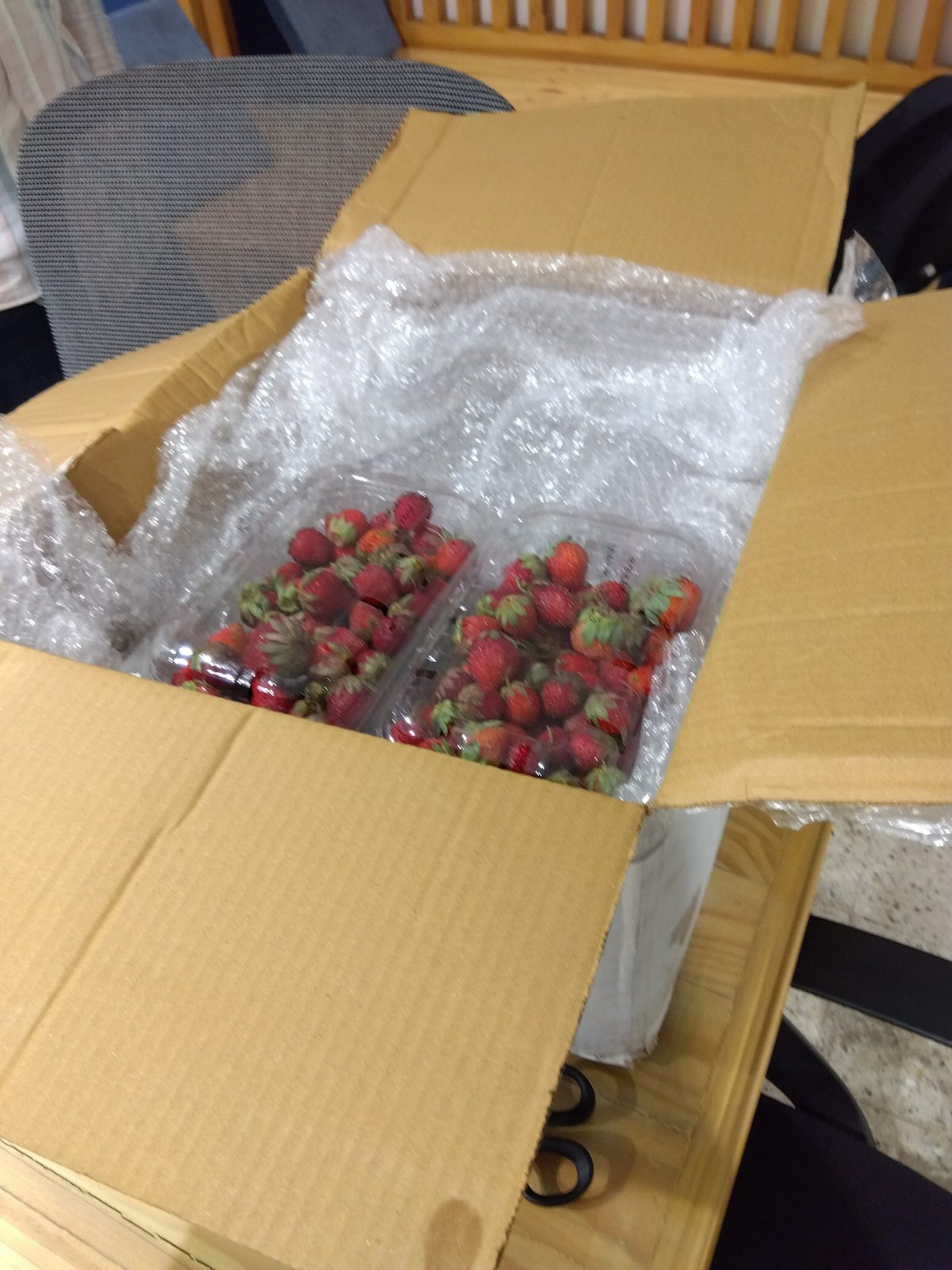 Strawberries in clear clamshell punnets, bubble-wrapped and nested inside a cardboard shipping box on a packing table
